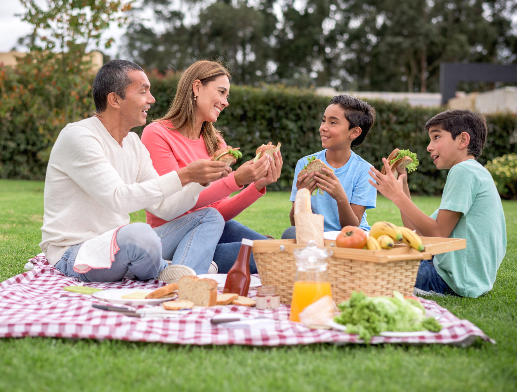 Happy family eating sandwiches at a picnic outdoors at the park and smiling